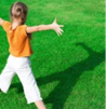 a child standing on grass with their arms outstretched looking at their shadow in front of them